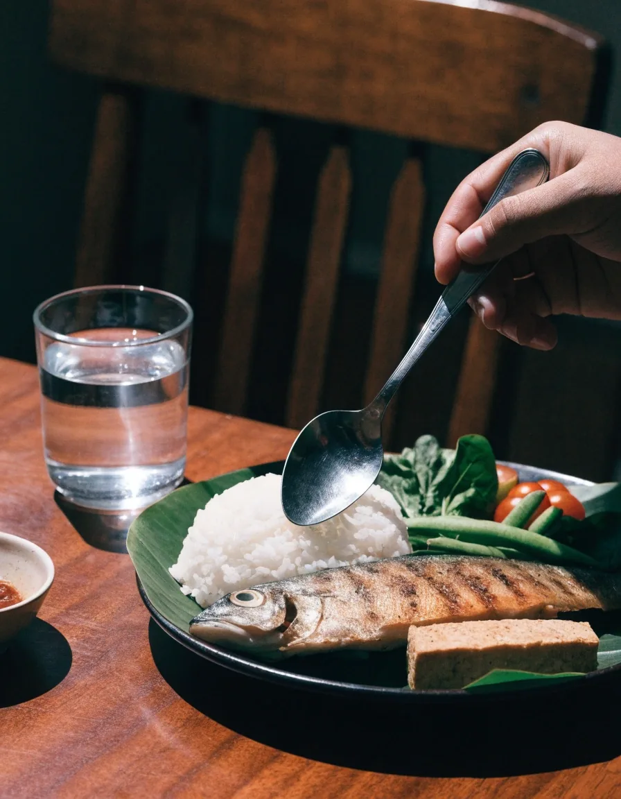 An Indonesian meal spread of rice, tempeh, greens and grilled fish arranged on banana leaf plates